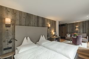 Chambre double moderne Rendl avec murs lambrissés, literie blanche, fauteuil violet et coin salon avec parquet.