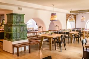 Speisesaal im Hotel Post am See Traunkirchen mit Holztischen, Bänken, Stühlen und einem großen grünen Kachelofen. Gewölbte Durchgänge sichtbar.