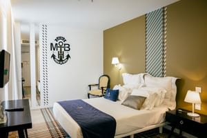 Modernes Doppelzimmer im Macarico Beach Hotel mit weißem Bett, nautischer Wanddekoration, geometrischen Mustern und zeitgemäßer Einrichtung.