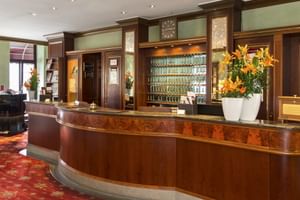 Elegante geschwungene Rezeption im Hotel Alte Post Konstanz mit dunkler Holzvertäfelung, grüner Marmorplatte, orangen Lilien und Einbauregalen.