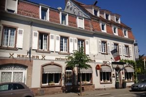 Bâtiment de trois étages de l'Hôtel Beauséjour à Colmar avec façade blanche, toit de tuiles rouges, volets traditionnels et restaurant au rez-de-chaussée.