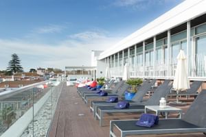 Moderne Dachterrasse im Hotel Baia in Cascais mit grauen Sonnenliegen, blauen Kissen, weißen Sonnenschirmen und Glasgeländer mit Stadtblick.