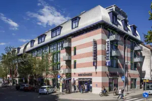 Modernes gestreiftes Gebäude des SEEhotel Friedrichshafen mit rot-weißer Fassade, Mansardendach und Balkonen an einem sonnigen Tag.