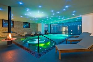 Moderner Spa-Wellnessbereich im Bad Horn Hotel mit beleuchtetem Innenpool, Entspannungsliegen, Kamin und blauer Ambientebeleuchtung.