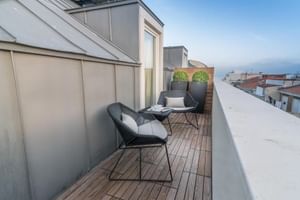 Moderne Dachterrasse im Universal Boutique Hotel mit Holzdielen, zwei schwarzen Stühlen, kleinem Tisch und Pflanzgefäßen mit Stadtblick.