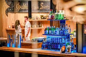 Bar d'hôtel moderne avec comptoir en bois, éclairage LED bleu, vaste présentation de bouteilles et enseigne 'Gasthof zum Stern'.
