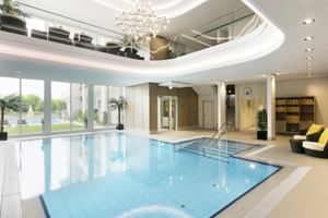 Modernes Hallenbad im Hotel Reutemann Lindau mit Glasdecke, weißen Säulen, zeitgenössischem Kronleuchter und Loungebereich.