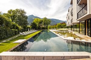 Moderner Außenpool im Hotel Sand mit Liegestühlen auf grüner Wiese, umgeben von Bergen und Bäumen in Südtirol.