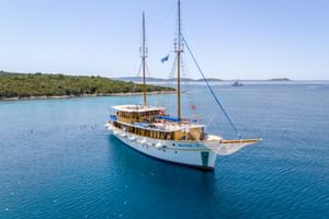 Weißes Motorsegelschiff MS Macek mit zwei Masten vor Anker in türkisfarbenem Adriatischem Meer nahe grüner kroatischer Küste.