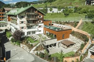 Vue aérienne de l'hôtel Schwarzer Adler à St. Anton avec architecture alpine traditionnelle, extension spa moderne et terrasse.