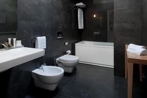 Modernes Badezimmer im Furadouro Beach & Spa mit dunklen Steinwänden, weißer Badewanne, WC, Bidet, schwebendem Waschbecken und Holzhocker.