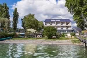 Außenansicht des Hotels Residenz Seeterrasse Wangen mit weißer Fassade und blauem Dach, direkt am Seeufer gelegen mit Terrasse und Steg.
