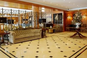 Luxuriöse Lobby des Hotel Moliceiro Aveiro mit Marmorböden, verzierten Eisengeländern, beigem Chesterfield-Sofa und Blumenarrangement.