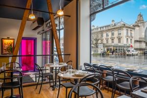 Modernes Bar-Interieur mit schwarzen Bistrostühlen, runden Tischen, sichtbaren Holzbalken und bodentiefen Fenstern mit Blick auf eine Straße in Tours.