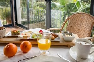 Petit-déjeuner avec oranges fraîches, jus d'orange, café et pâtisseries variées sur une table donnant sur un jardin tropical à Sóller.