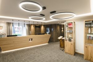 Réception d'hôtel moderne au Schwarzer Adler St. Anton avec comptoir en bois, éclairage circulaire et présentoirs.