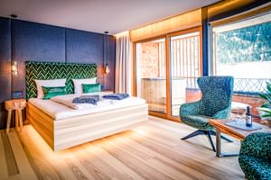 Chambre double élégante avec tête de lit géométrique verte, fauteuil bleu, parquet et portes-fenêtres donnant sur la montagne.