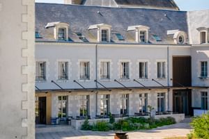 Weißes Steingebäude des Hotel Fleur de Loire in Blois mit grauem Schieferdach, Dachgauben und Terrasse mit Markisen zu einem sonnigen Innenhof.