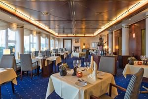 Eleganter Speisesaal im Bad Horn Hotel mit weißen Tischdecken, gestreiften Stühlen, blauem Teppich und großen Fenstern mit Seeblick.