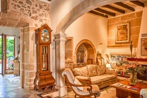 Hall d'entrée rustique avec murs en pierre, poutres apparentes, arches, horloge comtoise et meubles classiques au Son Sant Jordi Pollenca.