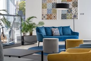 Moderne Lobby des Hotel Jupiter Lisboa mit blauem Sofa, gelbem Sessel, dekorativer Fliesenwandkunst, Palme und schwarzer Stehlampe.