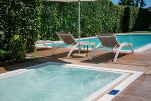 Hotel Palazzo del Garda Poolbereich mit sprudelndem Whirlpool im Vordergrund, zwei Liegestühlen unter Sonnenschirm auf Holzdeck und Hauptpool dahinter.