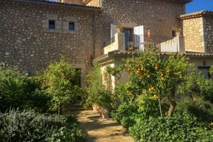 Bâtiment en pierre de Can Quatre à Sóller avec chemin de jardin traversant des orangers chargés de fruits et plantes méditerranéennes sous ciel bleu.