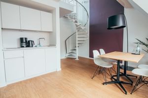 Moderne Hotel Upstalsboom Küche mit weißen Schränken, Esstisch mit weißen Stühlen und geschwungener Wendeltreppe. Lila Akzentwand sichtbar.