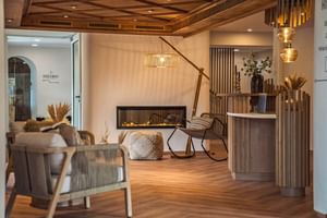 Moderne Hotelrezeption im Bergrose Strobl mit Holzrezeption, zeitgemäßem Sitzbereich, Kamin und warmer Beleuchtung.