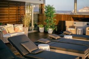 Moderne Terrasse im Macarico Beach Hotel mit dunklen Sonnenliegen, Korbmöbeln, Topfpflanzen und Holz-Sichtschutz mit Meerblick.