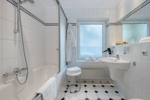Modernes Badezimmer mit weißen Fliesen, Badewanne mit Glasabtrennung, Waschbecken, Spiegel und schwarz-weißen Bodenfliesen im Salzburger Hof.