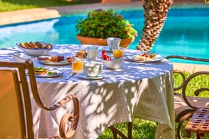Table de petit-déjeuner avec jus d'orange, café, pâtisseries et œufs près d'une piscine turquoise à Son Sant Jordi, Pollença.