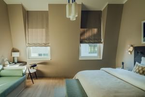 Modernes Deluxe Doppelzimmer im Hotel zum Hirschen mit beigen Wänden, weißem Bett, grüner Sitzecke, Holzboden und Pendelleuchten.