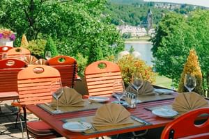 Hotelterrasse mit gedecktem Esstisch und orangen Stühlen mit Blick auf den Rhein und die Koblenzer Stadtlandschaft mit historischen Gebäuden.