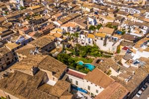 Vue aérienne de Son Sant Jordi à Pollença montrant des bâtiments traditionnels aux toits de tuiles, une piscine centrale entourée de jardins et cyprès.