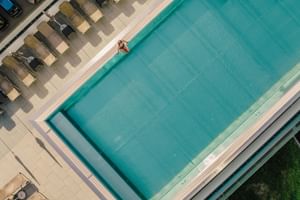 Luftansicht des Mein Almhof Skypools mit türkisfarbenem Wasser, umgeben von beigen Sonnenliegen und Sonnenschirmen auf hellem Deck.