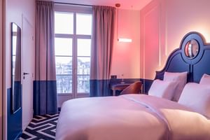 Modernes Doppelzimmer in Rosa und Blau mit Bett mit dekorativem Kopfteil, französischen Türen und geometrischem Bodenmuster.