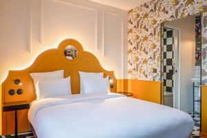 Modernes Doppelzimmer mit markanter orangefarbener geschwungener Kopfteil, weißer Bettwäsche, Blumentapete und eigenem Bad im Hotel Labe Tours.