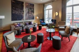 Moderne Hotellobby mit rotem Teppich, grauen Sitzgelegenheiten, schwarzen runden Tischen, großen Bogenfenstern und zeitgenössischer Kunst.