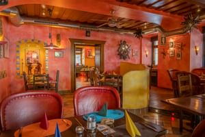 Innenraum des Restaurants El Venado mit warmen orangefarbenen Wänden, sichtbaren Holzbalken, roten Lederstühlen und bunten Tischdekorationen.