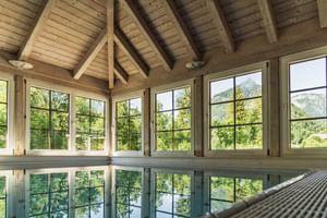 Innenpool des Bergrose Hideaway mit sichtbaren Holzbalken an der Decke und großen Fenstern mit Blick auf grüne Berge und Waldlandschaft.