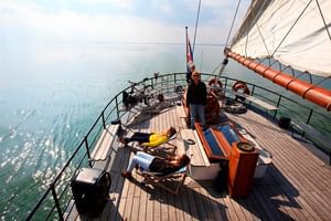 Holzdeck des Segelschiffs Wapen fan Fryslan mit Passagieren auf Liegestühlen, weiße Segel sichtbar, ruhige See im Hintergrund.