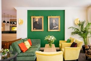 Hotel Reutemann Lindau Lobby mit grüner Akzentwand, historischen Porträts, grünem Sofa mit bunten Kissen, gelben Sesseln und Pflanzen.