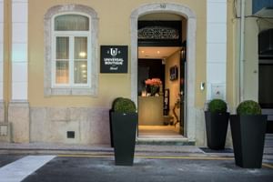 Eingang zum Universal Boutique Hotel mit schwarzem Schild, Steinbogen und drei großen Pflanzgefäßen mit Buchsbäumen auf dem Gehweg.