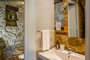 Modernes Bad im Le Valli Agriturismo mit weißem Waschbecken, Spiegel und freiliegenden Steinwänden. Holzbalken über dem Waschbecken mit Handtuchhalter.