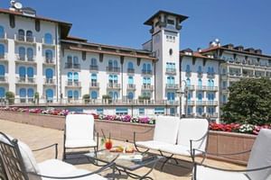 Elegante Terrasse im Hotel Savoy Gardone mit weißen Gartenmöbeln und bunten Blumenkästen, mit Blick auf das historische Hotelgebäude.