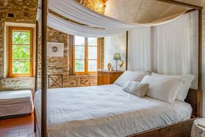 Doppelzimmer mit weißem Himmelbett, Steinwänden, Terrakottaboden und Holzfenstern im Agriturismo Le Valli in Casciana Terme, Toskana.