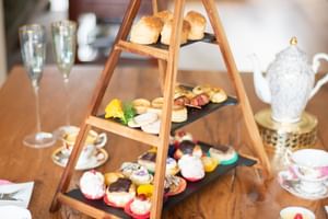 Hölzerner Etagenständer mit Scones, Gebäck und Kuchen auf einem Esstisch. Teetassen, Sektgläser und Beilagen vervollständigen das Afternoon-Tea-Setup.