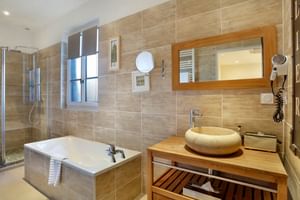 Modernes Badezimmer mit Holzoptik-Fliesen, Badewanne, Glasdusche, Holzwaschtisch mit cremefarbenem Aufsatzwaschbecken im Auberge du Bon Laboureur.