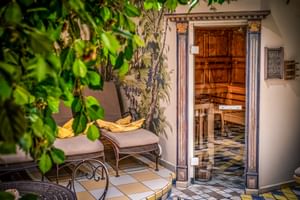 Espace bien-être avec porte de sauna en verre, colonnes décoratives, chaise de relaxation avec serviette jaune et plantes vertes luxuriantes.